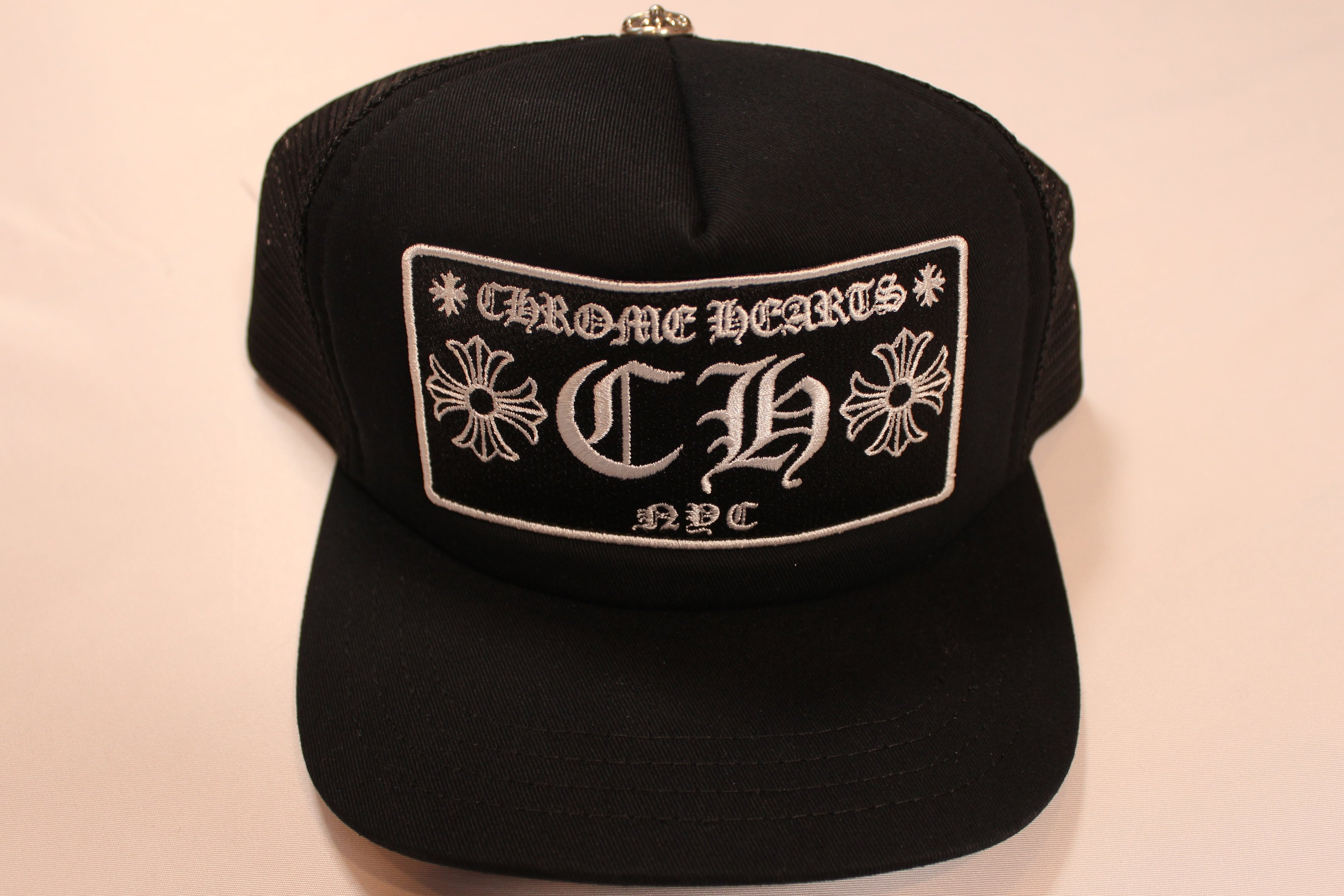 Black cap with 'Chrome Hearts' logo on a beige background