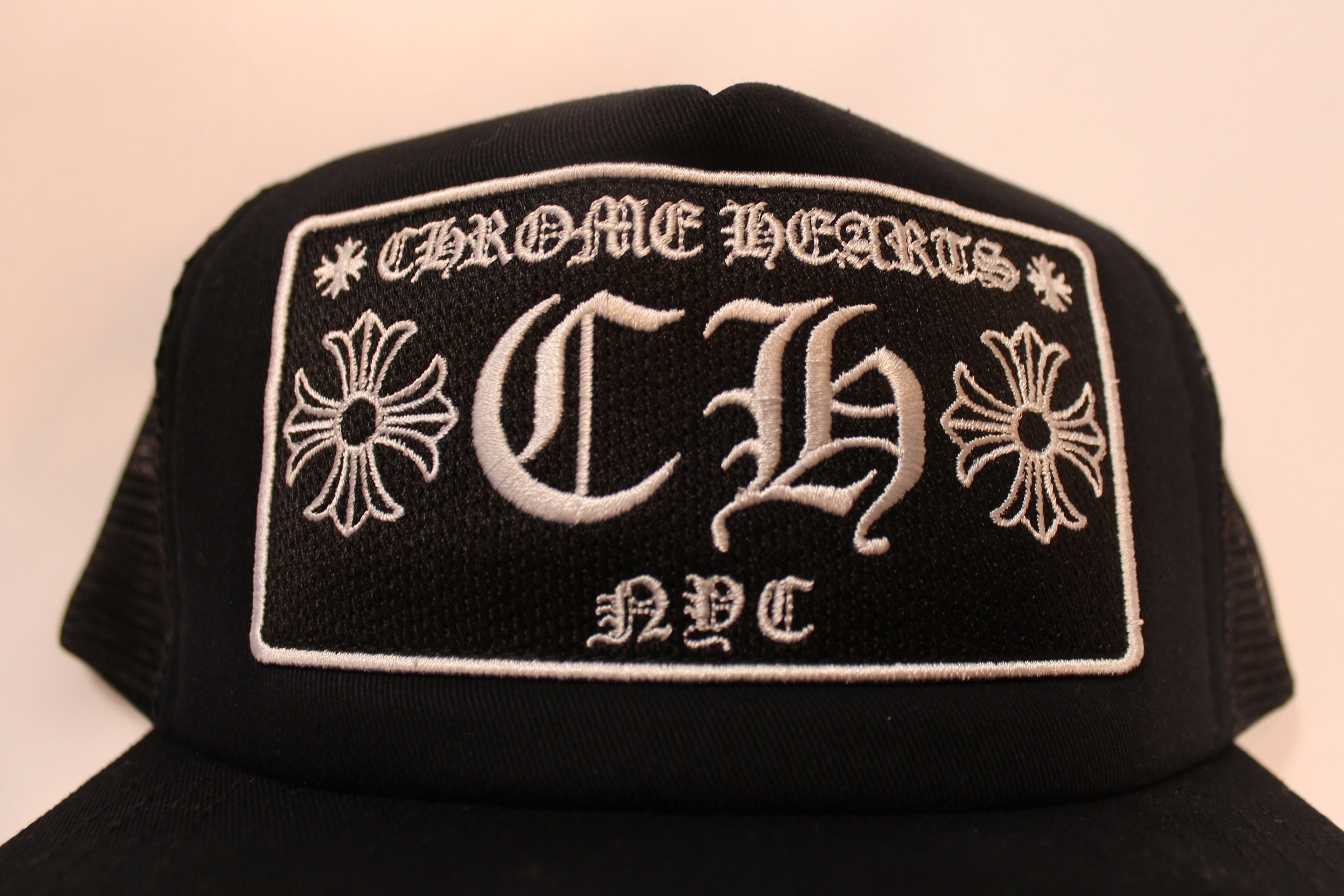 Black cap with embroidered logo and text on a beige background